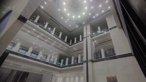 Un atrio de varios niveles con un espacio central abierto, barandillas de vidrio y un techo decorativo.