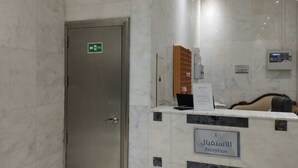Zona de recepción con pared de mármol, mostrador de recepción, una computadora y un cartel que indica la recepción.