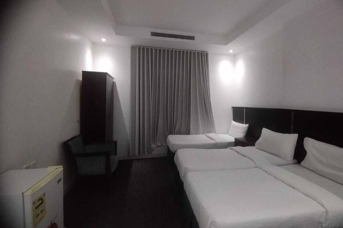 A hotel room with two single beds, a small bedside table, a TV, and a window with curtains.