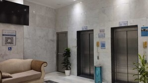 Un vestíbulo con un sofá, plantas en macetas y dos ascensores.