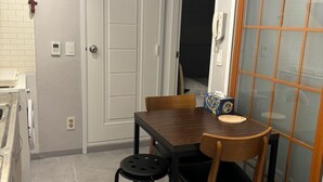 Cocina compacta con comedor, lavadora y puerta corrediza de vidrio que da a una habitación oscura.