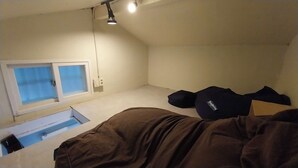 Una habitación pequeña y con poca luz, con una cama individual, un ventanal y una lámpara en el techo.