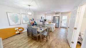 A modern kitchen with white cabinetry, a dining area with a wooden table and chairs, and a ceiling light fixture.
