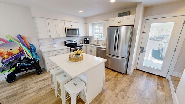 A modern kitchen with white cabinetry, stainless steel appliances, and a central island with stools.