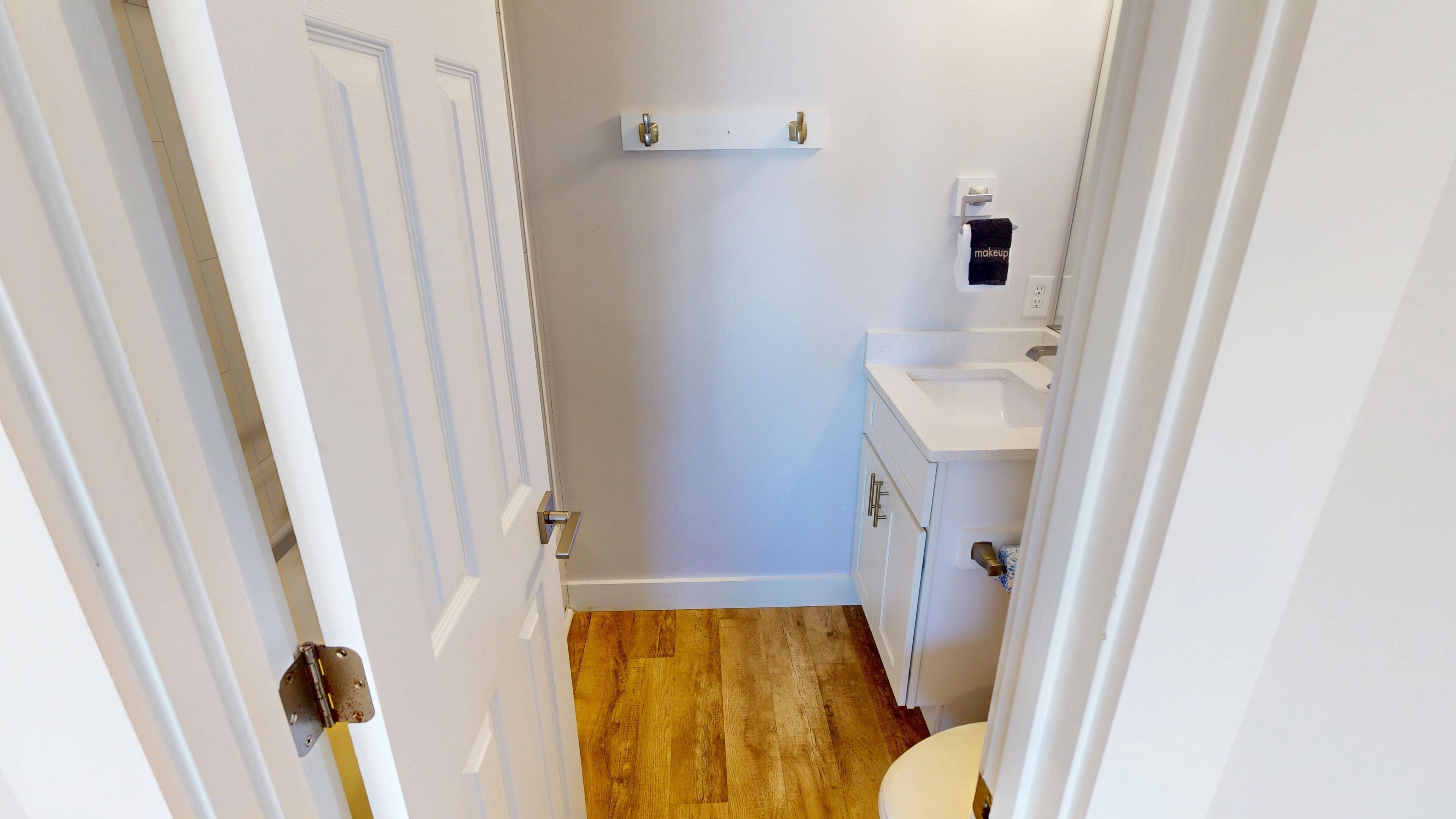 A narrow bathroom with a wooden floor, a white sink, and a towel rack.