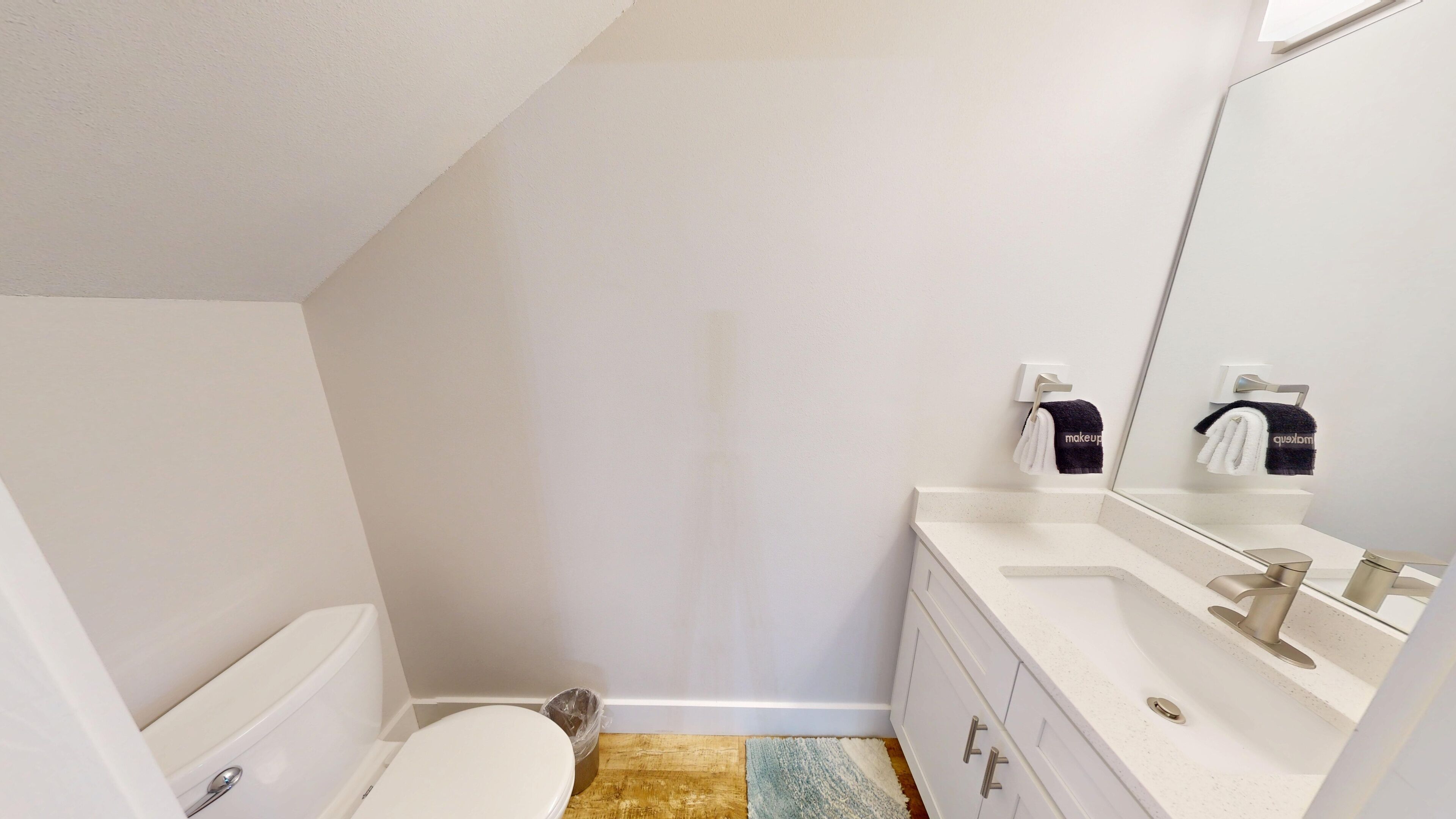 A small, modern bathroom with a white toilet, a sink with a mirror, and a towel rack with two towels.
