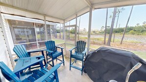 A covered patio area with blue Adirondack chairs and a grill.