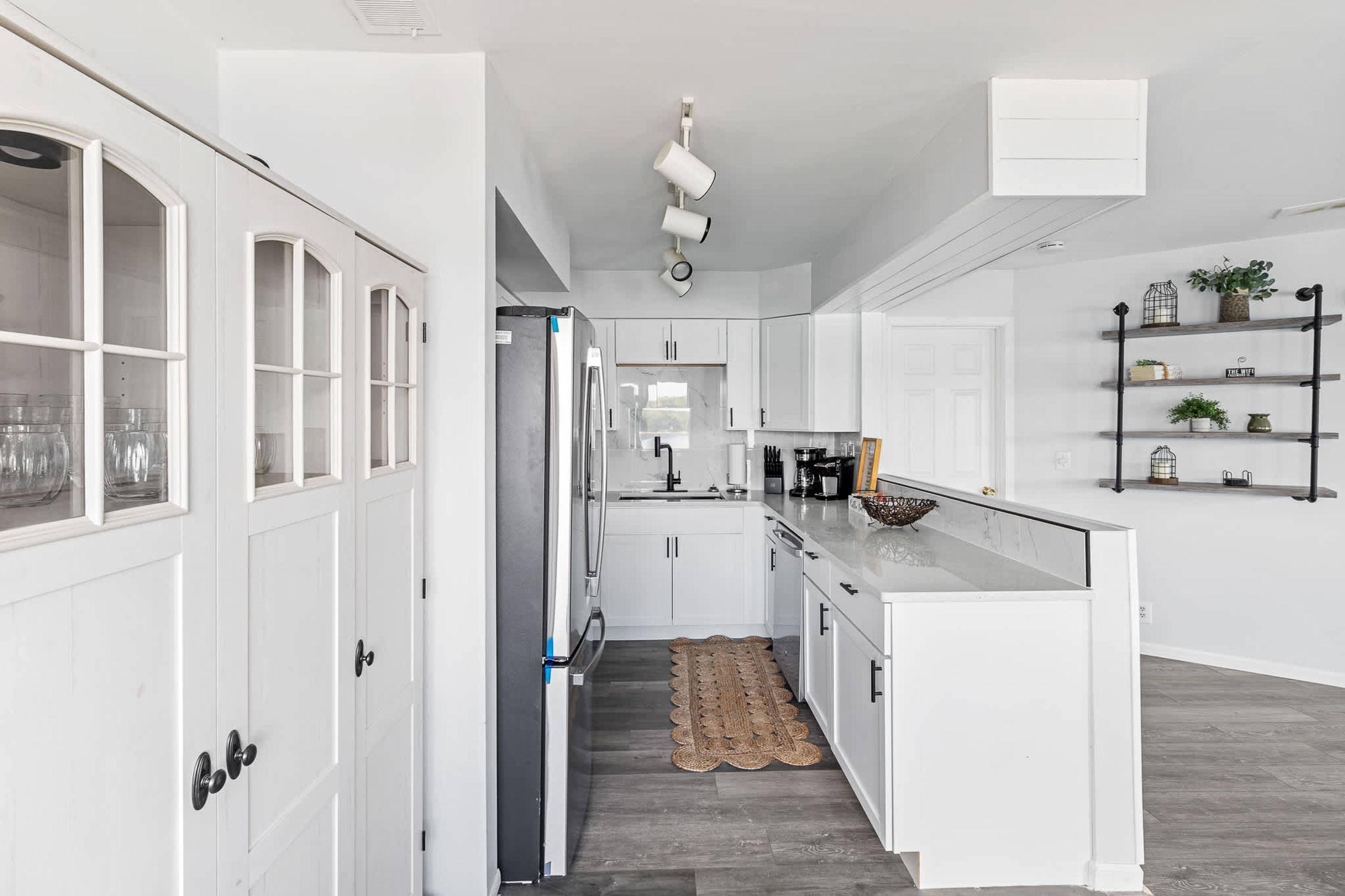A modern kitchen with white cabinetry, a central island, and a wooden floor rug.