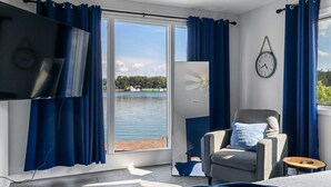 A bedroom with a large window, a bed, a chair, a small table, and a wall clock. - Renovated River Home Hot Tub Sauna Game Room (Jeffersonville)