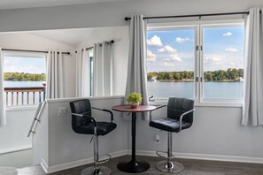 A room with a view of a lake, two black chairs, a small table with a plant, and a window with curtains. - Renovated River Home Hot Tub Sauna Game Room (Jeffersonville)