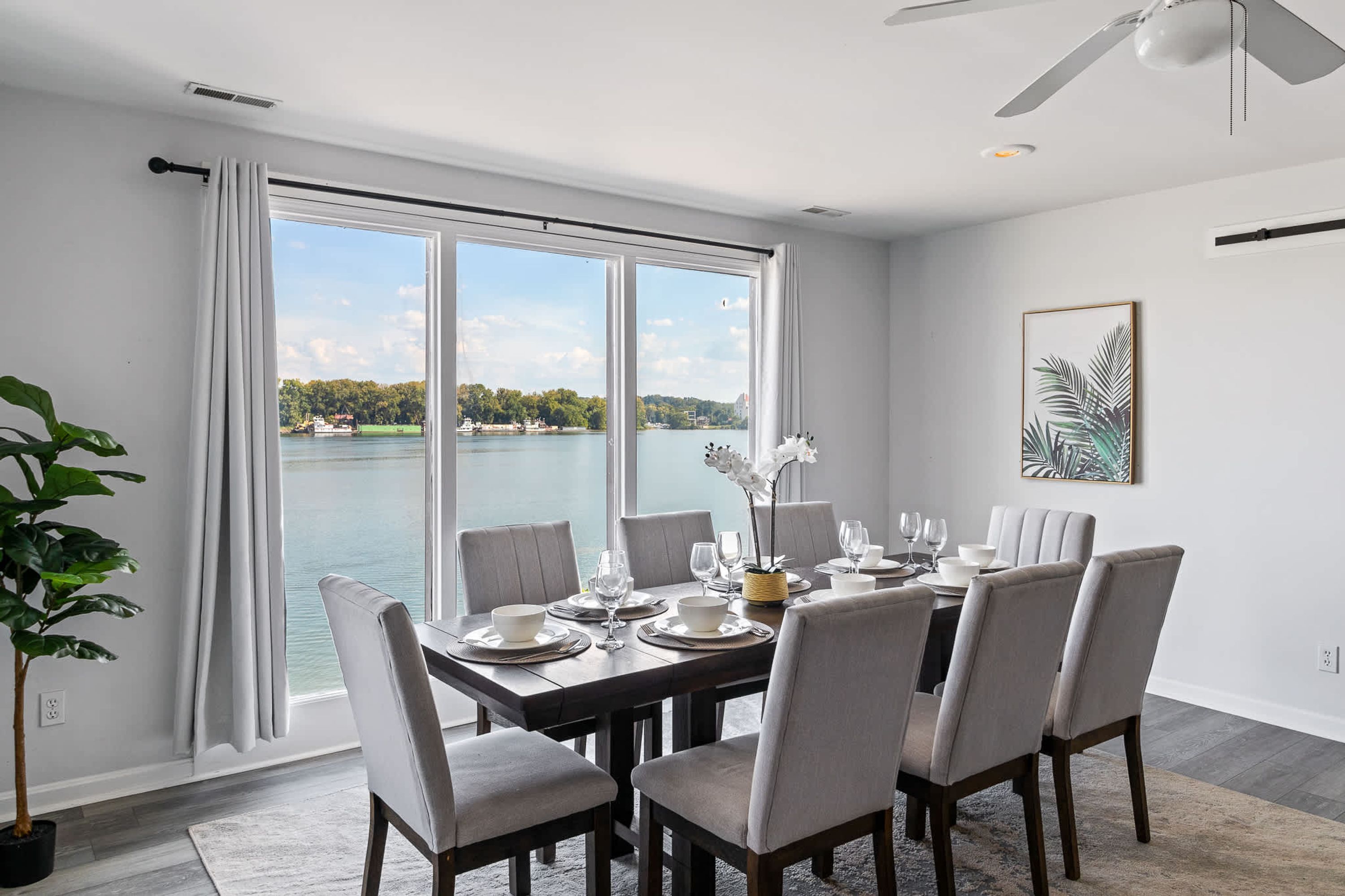 A dining area with a view of a lake, a ceiling fan, and a framed plant.