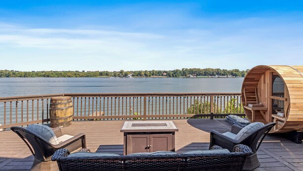 A wooden deck with wicker furniture, a hot tub, and a view of a lake. - Renovated River Home Hot Tub Sauna Game Room (Jeffersonville)