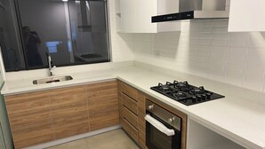 A modern kitchen with wooden cabinets, a stainless steel sink, a black stove, and a window above the sink. - Elegant and Centrally Located Vallecito Apartment (Arequipa)