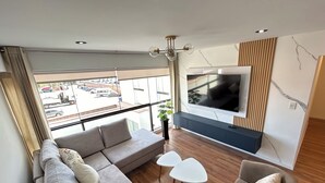 A modern living room with a large TV, a sofa, a chair, and a small table. - Elegant and Centrally Located Vallecito Apartment (Arequipa)