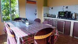 Un comedor con una mesa cubierta por un mantel estampado, rodeado de sillas. Se ve una cocina al fondo con armarios y un microondas.