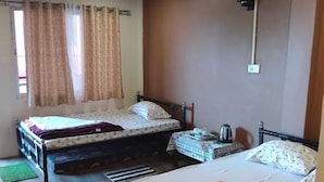 Una habitación con dos camas, una mesita y un ventanal con cortinas.