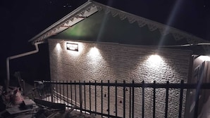 Un pequeño edificio rústico con fachada de piedra y techo de metal, iluminado por luces exteriores.