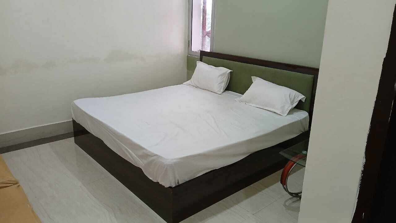 Un letto singolo con una testiera verde in una stanza dalle pareti spoglie e pavimento piastrellato.