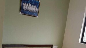 A neatly made bed with white linens in a room with a green wall and a framed picture above it.