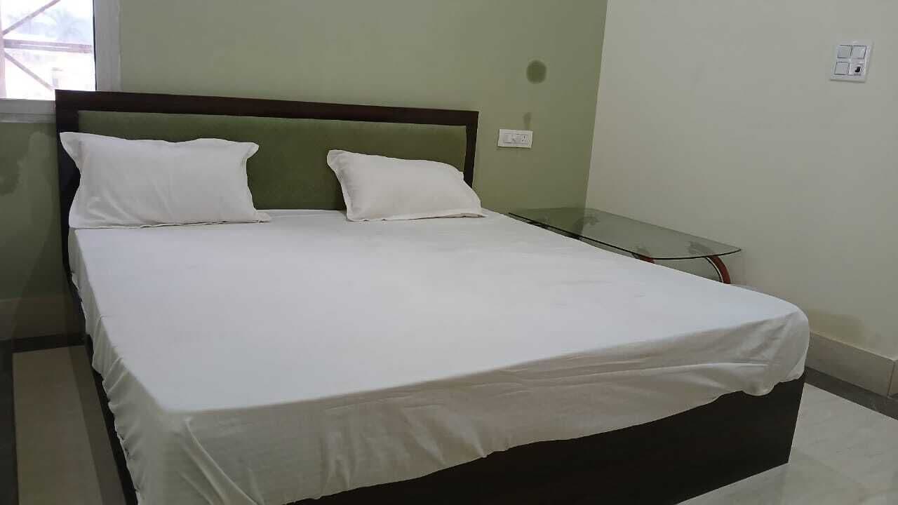 Una cama bien hecha con sábanas blancas en una habitación con pared verde y una mesita de noche de vidrio.