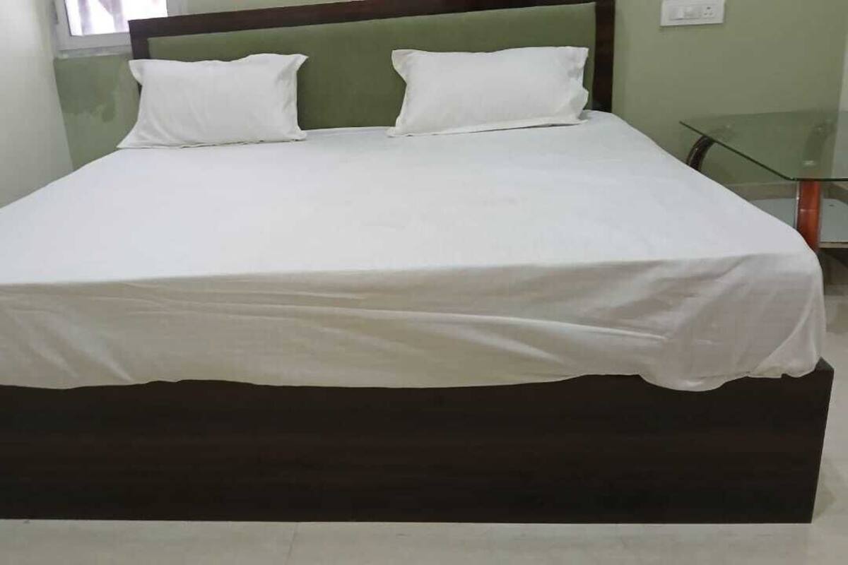 Een bed met een donker houten frame en witte beddengoed in een kamer met een glazen tafel en een groene wand.