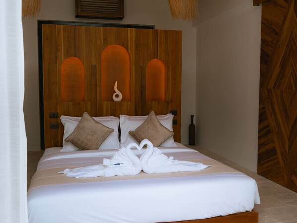 Habitación de hotel con cabecera de madera, ropa de cama blanca y dos toallas con forma de cisne sobre la cama.