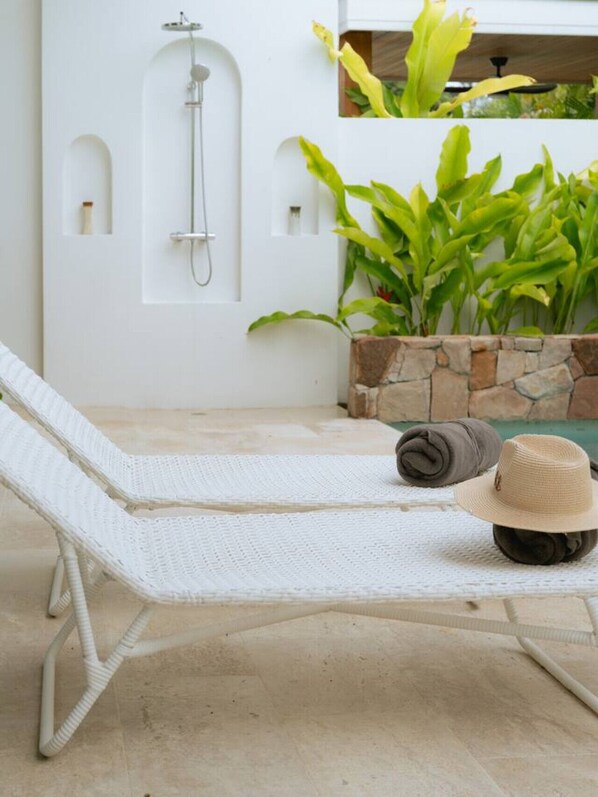 Una silla de lounge blanca con una jardinera de piedra y plantas tropicales cerca.