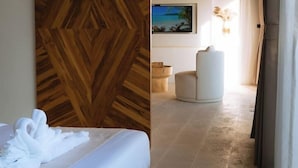 A hotel room with a bed, slippers, a wooden wall panel, a painting, a chair, and a view of the beach.