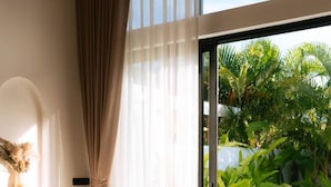 A modern room with a large window, a beige armchair, and a view of a swimming pool and greenery.