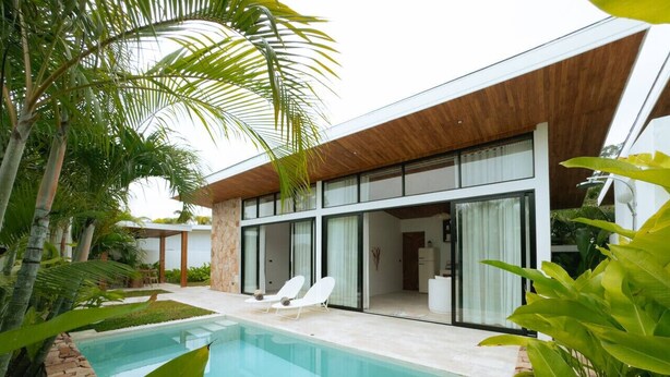 A modern house with a swimming pool, white lounge chairs, and a patio area surrounded by tropical plants.