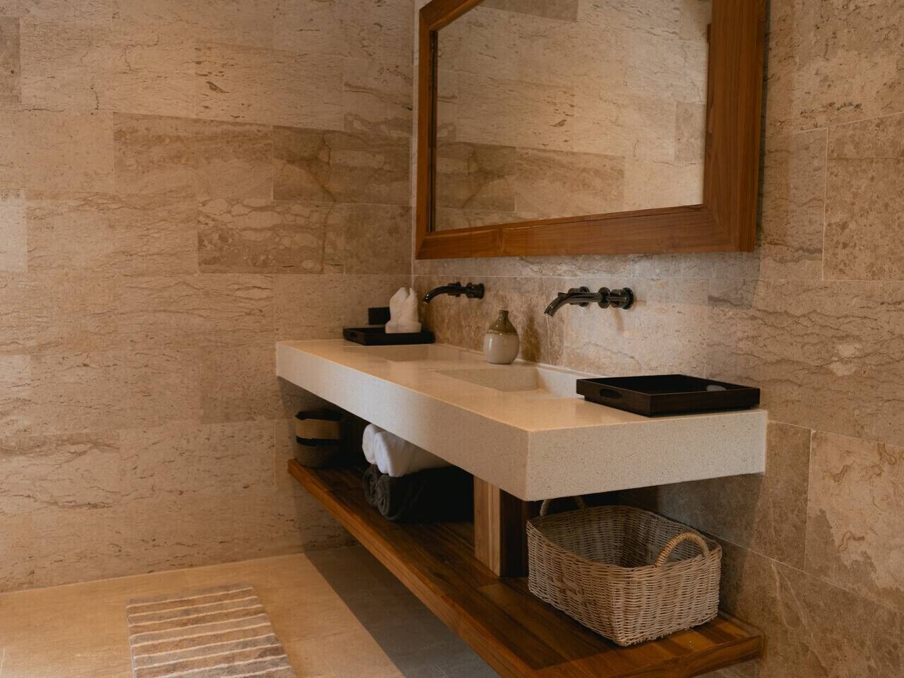 A bathroom with a stone wall, a wooden shelf, a white sink, a mirror, and a wicker basket.
