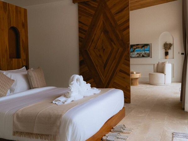 A hotel room with a large bed, a wooden accent wall, a painting, and a seating area with a chair and a small table.