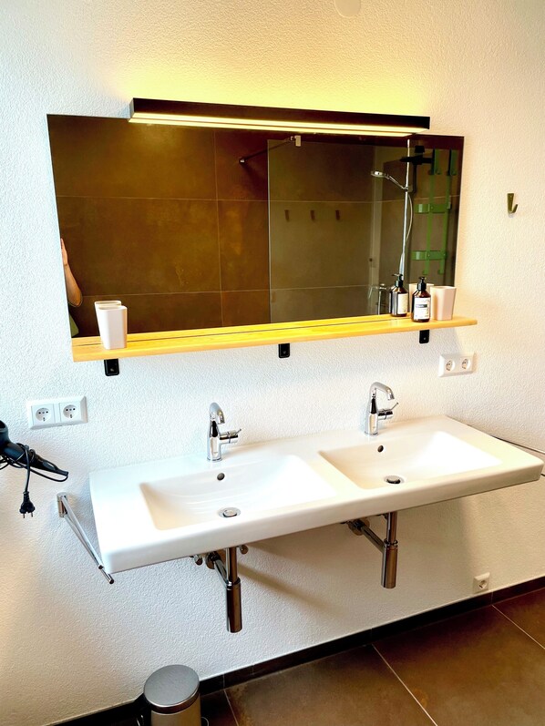 A bathroom with a double sink, a mirror above, and a shelf with toiletries. - New and Stylish Vacation Apartment (Yarin) (Lörrach)