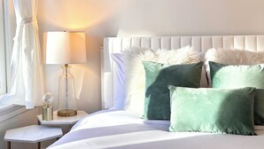 A neatly made bed with white bedding and green pillows, a bedside lamp, and a decorative glass object on a nightstand. - Downtown 1BR Retreat – Walk to PPAC – Kitchen & W/D (Providence)