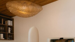 A modern living room with a round white sofa, a white armchair, a woven ceiling light, a bookshelf, a painting of a beach scene, and a small vase with dried plants. - 1 Bedroom Island Retreat central located (Bo Phut)
