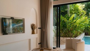 A modern living room with a round coffee table, a beige armchair, and a large window overlooking a pool and lush greenery. - 1 Bedroom Island Retreat central located (Bo Phut)