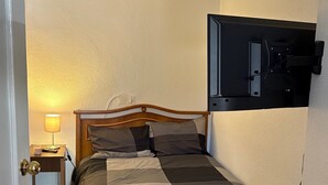 Une chambre à coucher comprenant un lit, une table de chevet, une lampe, un téléviseur fixé au mur et une commode en bois.