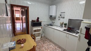 Une cuisine de taille réduite, avec des meubles blancs, une cuisinière à gaz, un four à micro-ondes et un chauffe-eau.