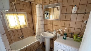 Une petite salle de bain comprenant des toilettes, un lavabo, une baignoire et un lave-linge.