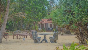 A beachside setting with a house, wooden furniture, and tropical vegetation. - Blue Water Paradise Akurala (Akurala)