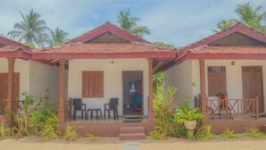 A row of small, single-story buildings with tiled roofs, each featuring a door and windows, and surrounded by plants and palm trees. - Blue Water Paradise Akurala (Akurala)