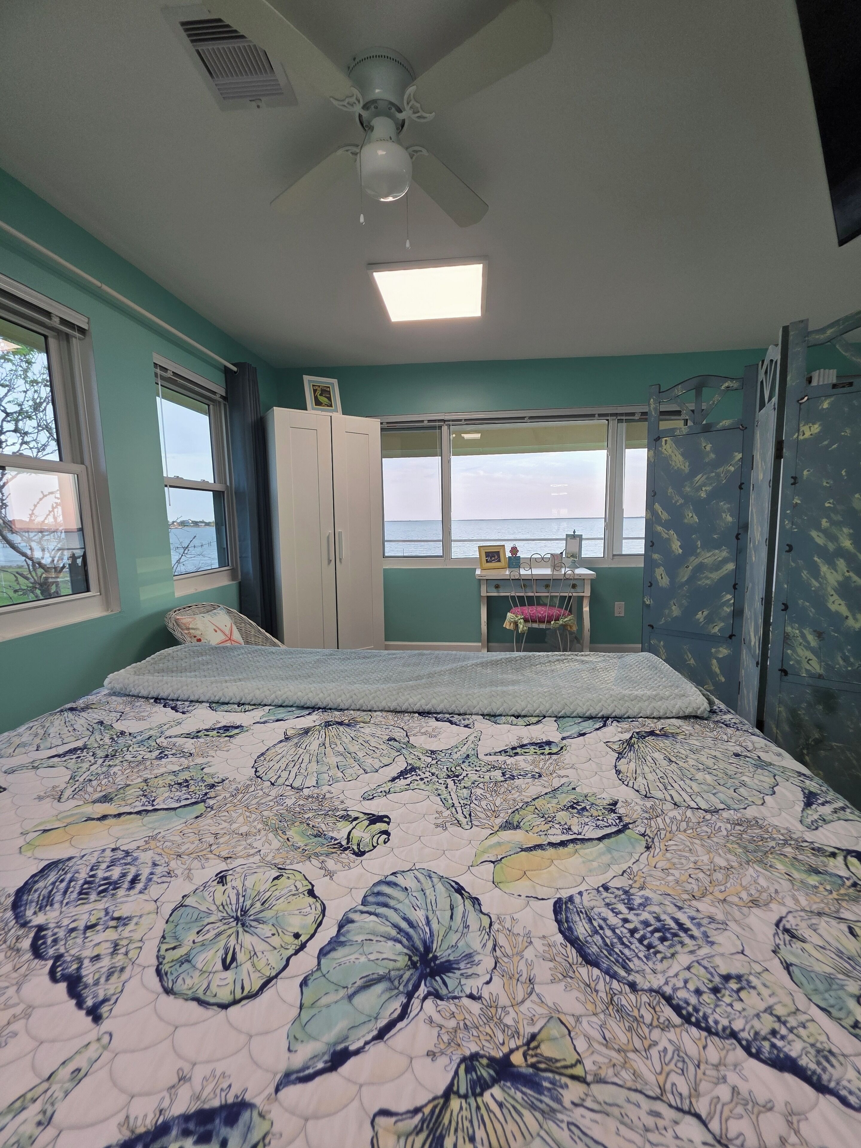 A bedroom with a bed, a ceiling fan, a window with a view of the sea, and a bunk bed.