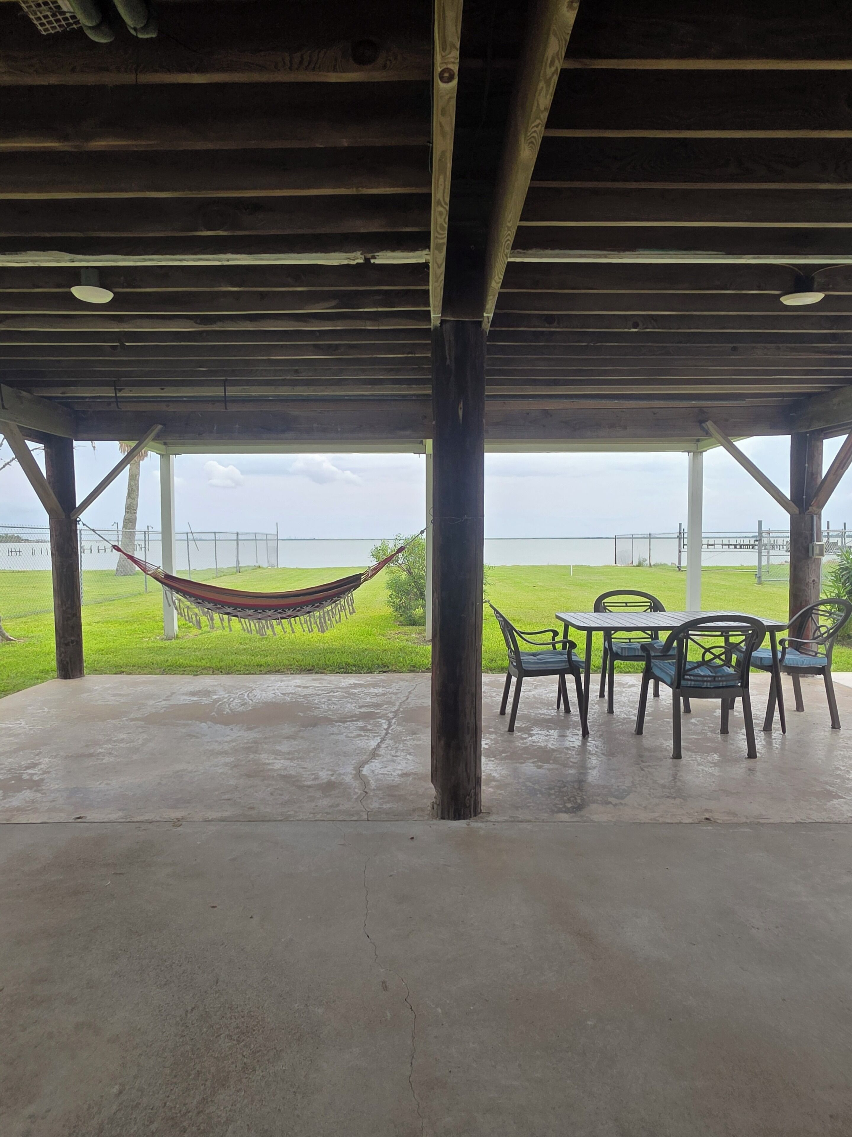 A covered outdoor area with a concrete floor, a hammock, and a table with chairs.