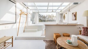 Een lichte, moderne badkamer met dakraam, een houten bankje, een rond tafeltje met waterkoker en uitzicht op de natuur.
