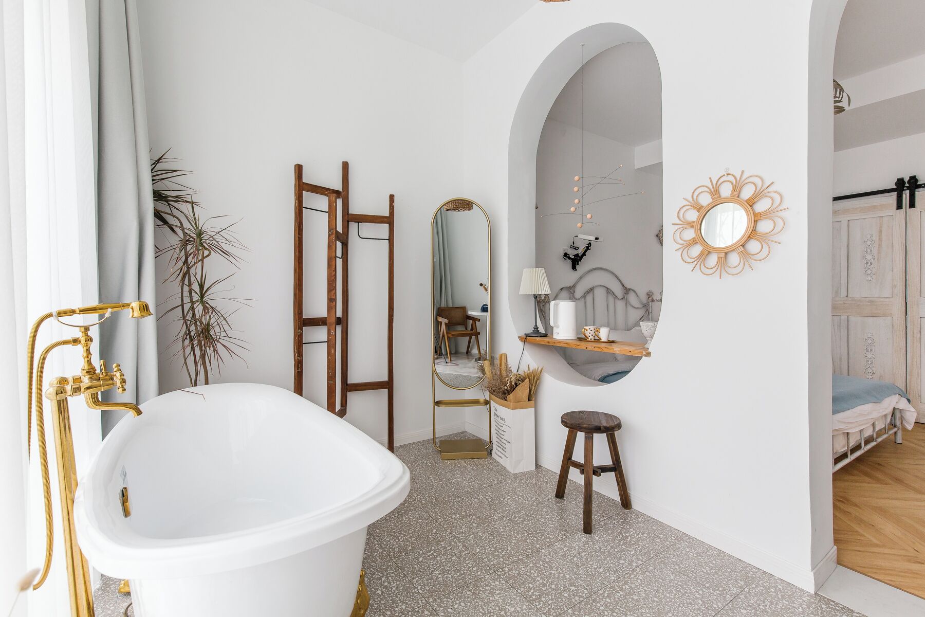 Ein Badezimmer mit freistehender Badewanne, einer Holzleiter, einem Spiegel und einem Waschtisch mit Hocker.