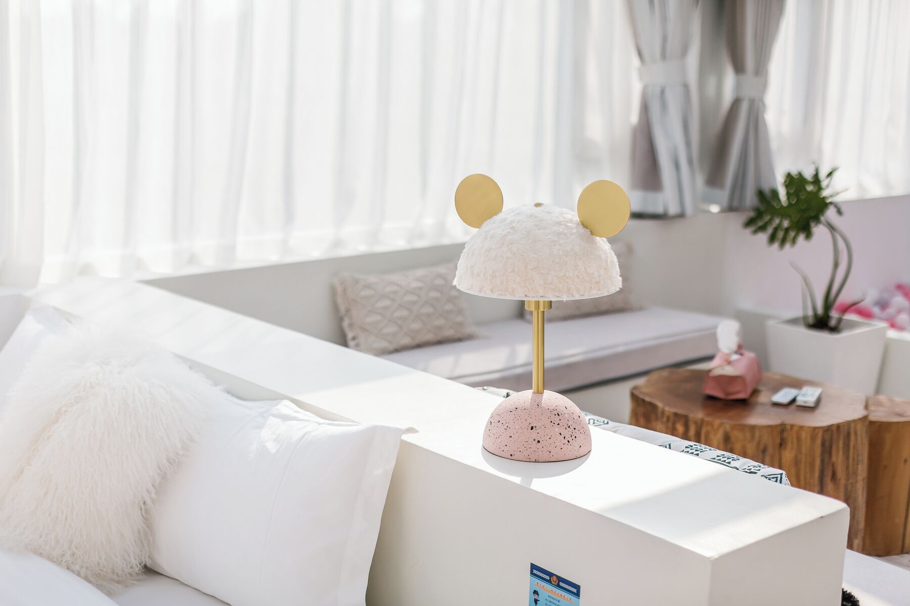A modern living room with a white sofa, a decorative lamp with a pink base, and a wooden side table with a pink object on it.