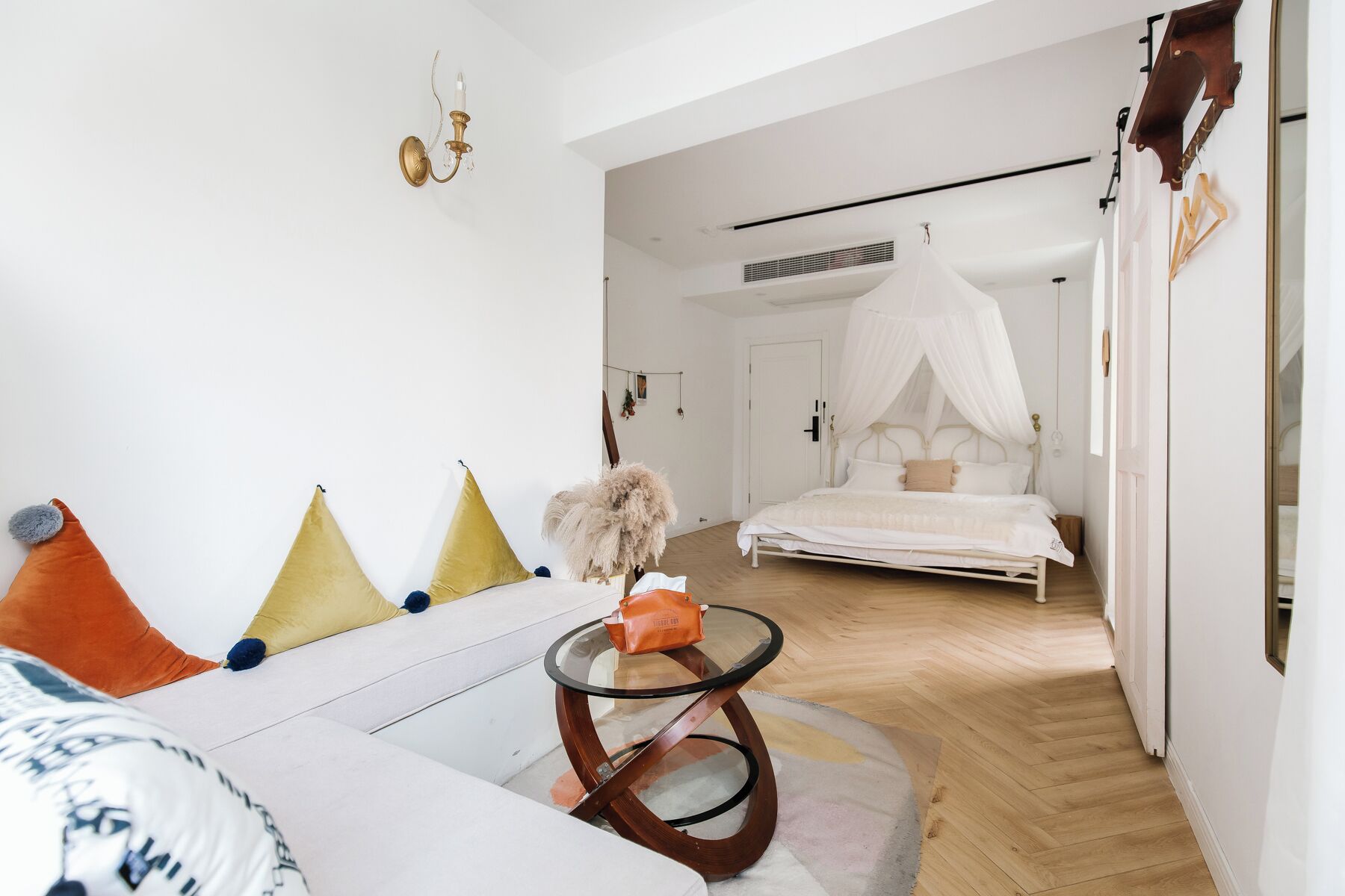 A modern bedroom with a canopy bed, a white sofa with colorful cushions, and a glass table.