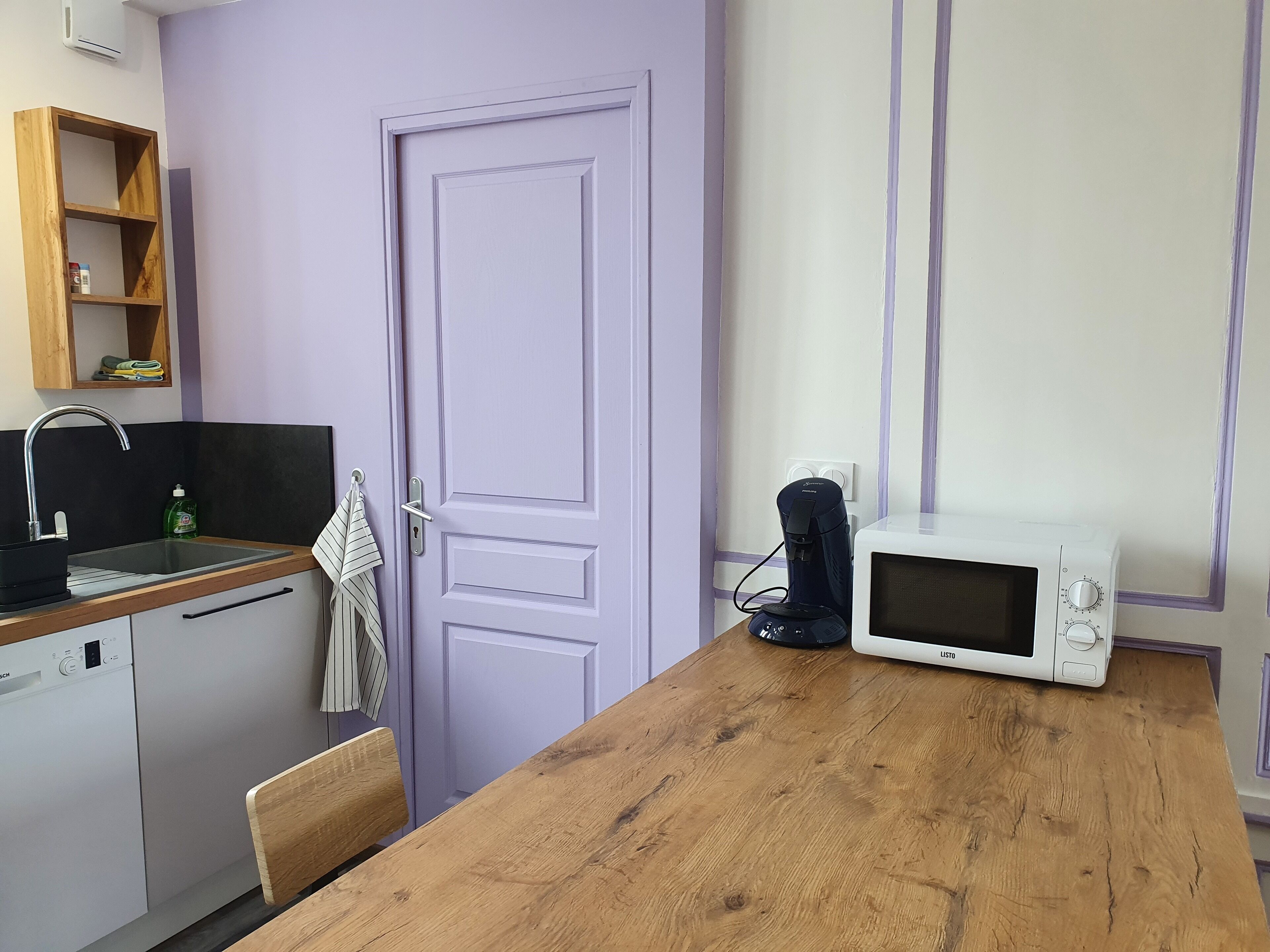 A compact kitchen with a wooden countertop, a sink, a dishwasher, a microwave, and a coffee maker.