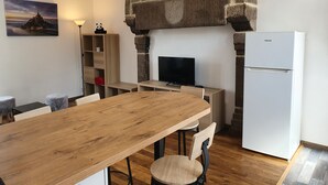 A modern kitchen with a stone arch, a wooden dining table, and a white refrigerator. - Fully furnished and equipped apartment in the courtyard of the Haut Manoir (Villedieu-les-Poêles)