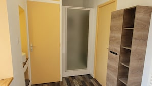 A hallway with a wooden floor, a yellow door, a frosted glass door, and a wooden shelving unit. - Fully furnished and equipped apartment in the courtyard of the Haut Manoir (Villedieu-les-Poêles)